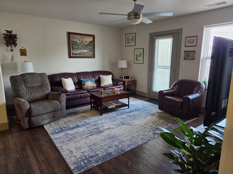 A living room with a brown leather couch, a grey armchair, a brown armchair, a coffee table, and a ceiling fan.